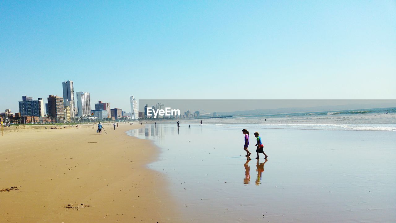 People walking at beach against clear sky