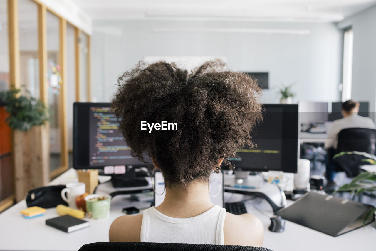 Female computer programmer with curly hair sitting at desk in office