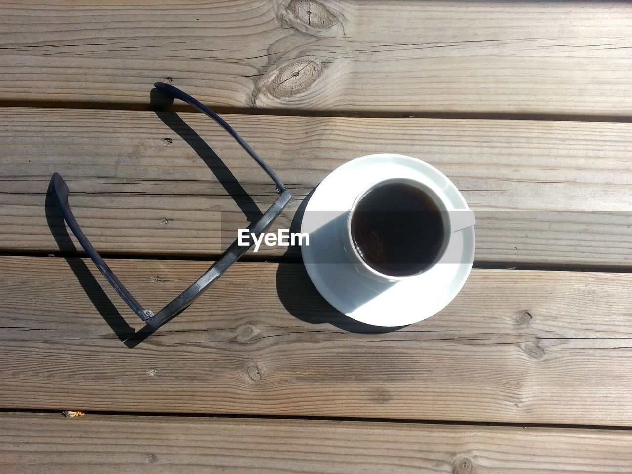 High angle view of coffee cup by eyeglasses on wooden table