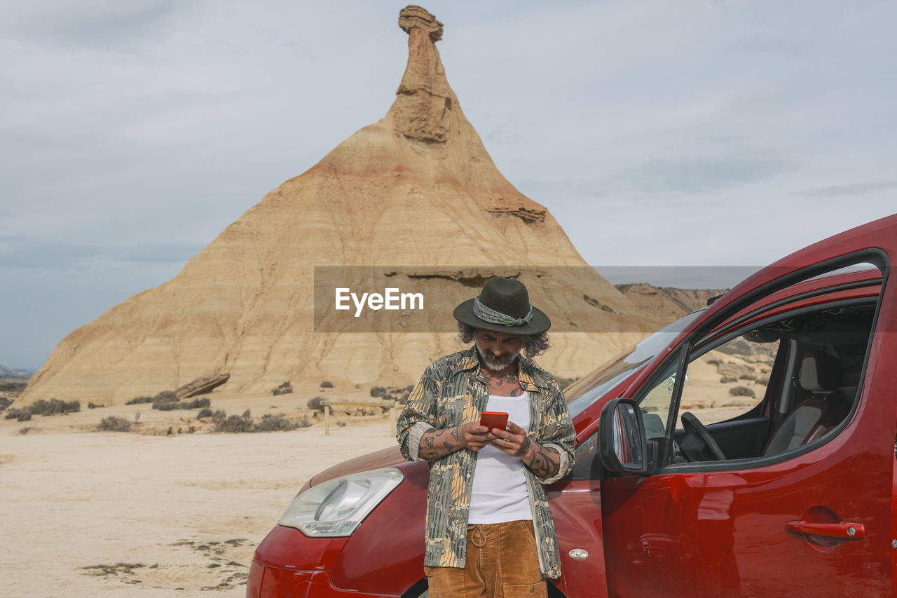 Middle aged traveler looking at cell phone in desert landscape of bardenas reales.