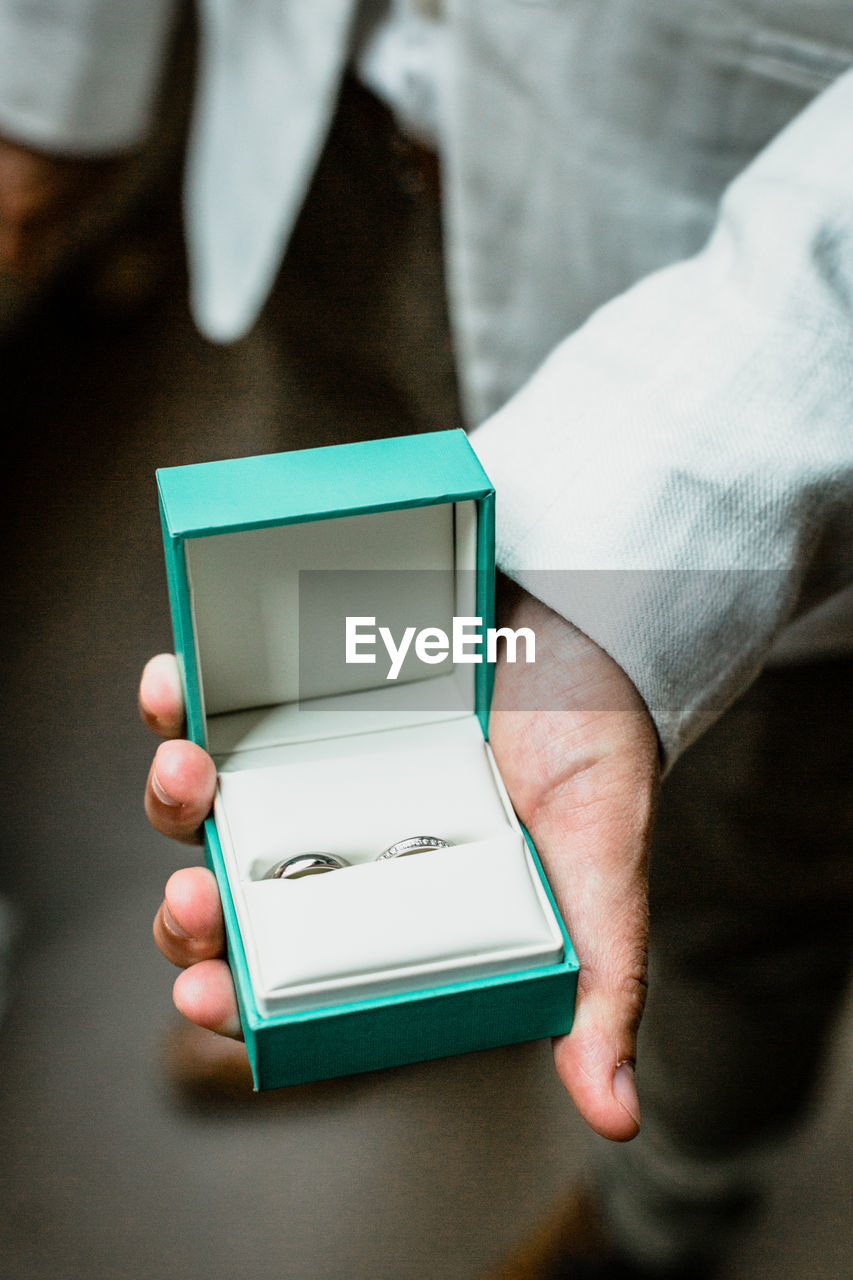 Low section of groom holding wedding rings while standing indoors