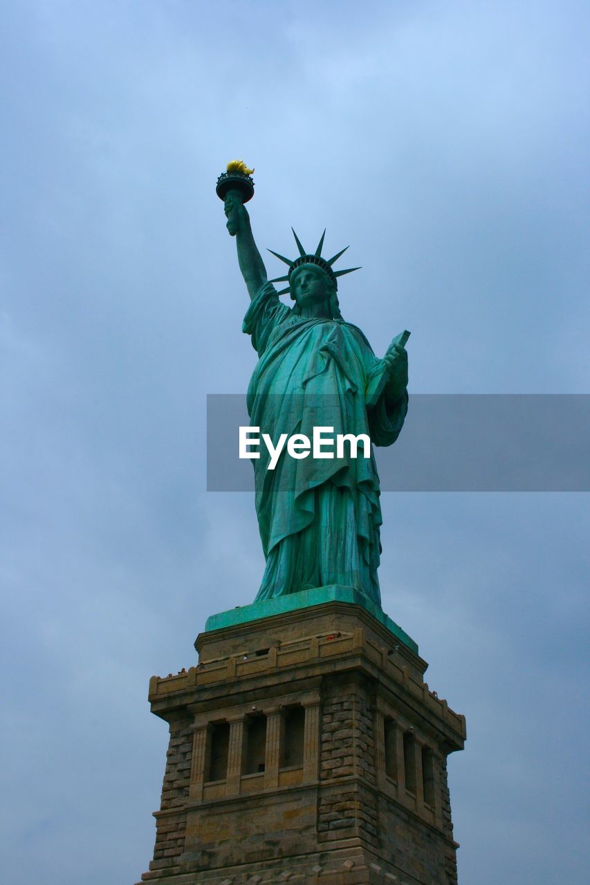 LOW ANGLE VIEW OF STATUE OF LIBERTY AGAINST CLOUDY SKY