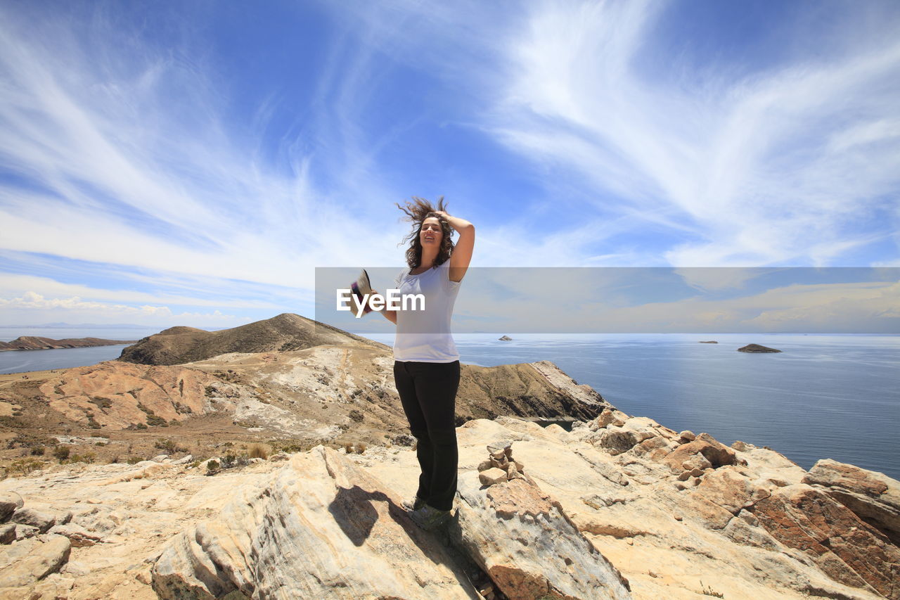 Full length woman standing on rock formation by lake titicaca against sky