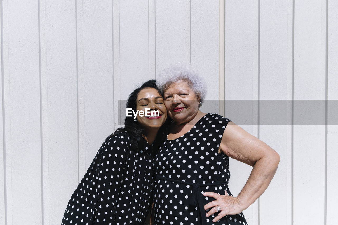 Mother and daughter standing cheek to cheek in front of wall