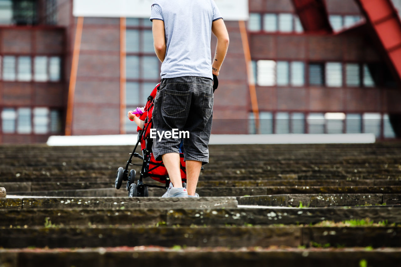 Low section of father pushing child in carriage on steps