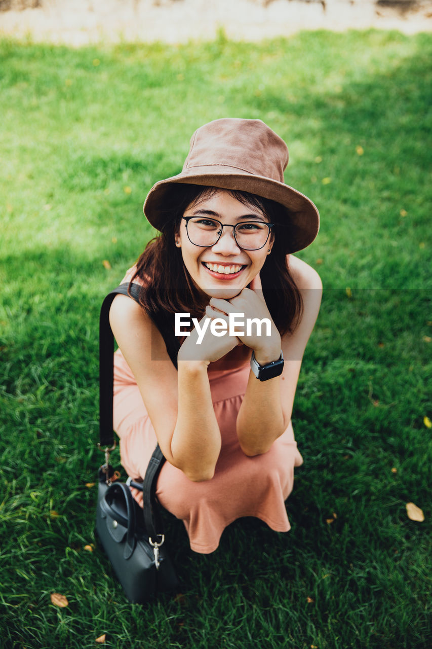 Portrait of asian young woman wearing glasses, brown dress and hat relaxing on the grass