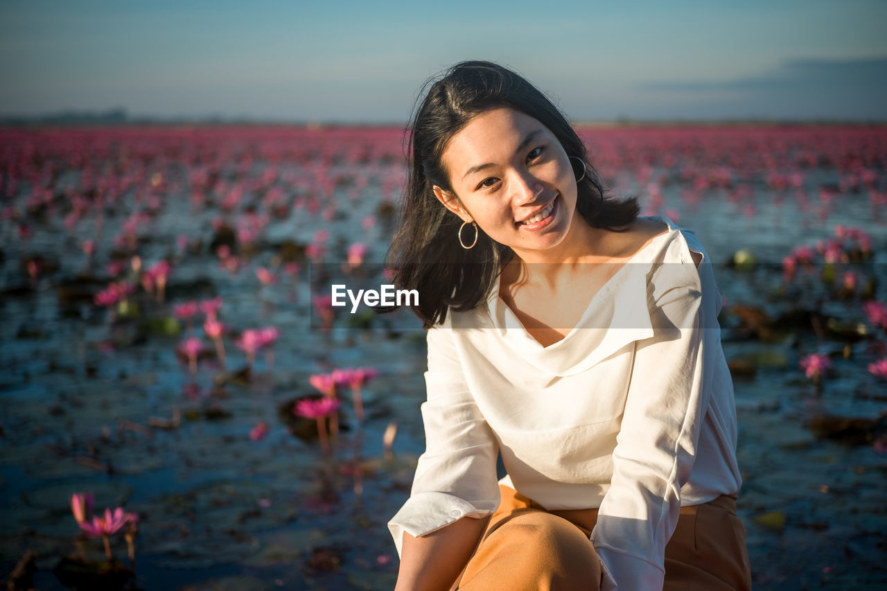 Portrait of young woman smiling while sitting against water lilies in pond