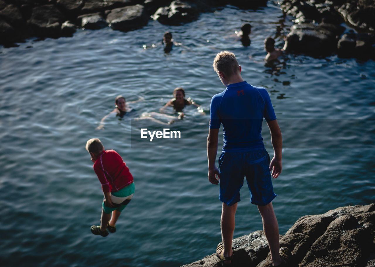 REAR VIEW OF PEOPLE ENJOYING ON ROCKS AT SEA