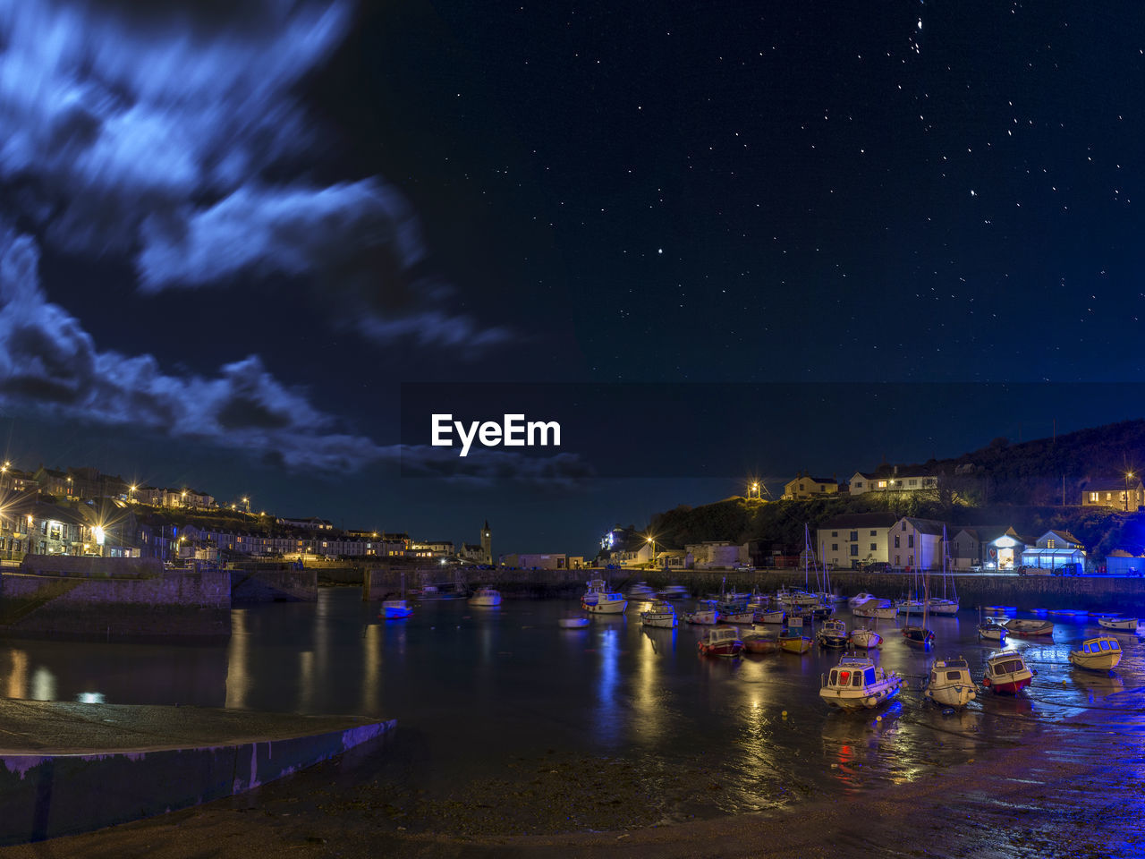 Illuminated city by sea against sky at night