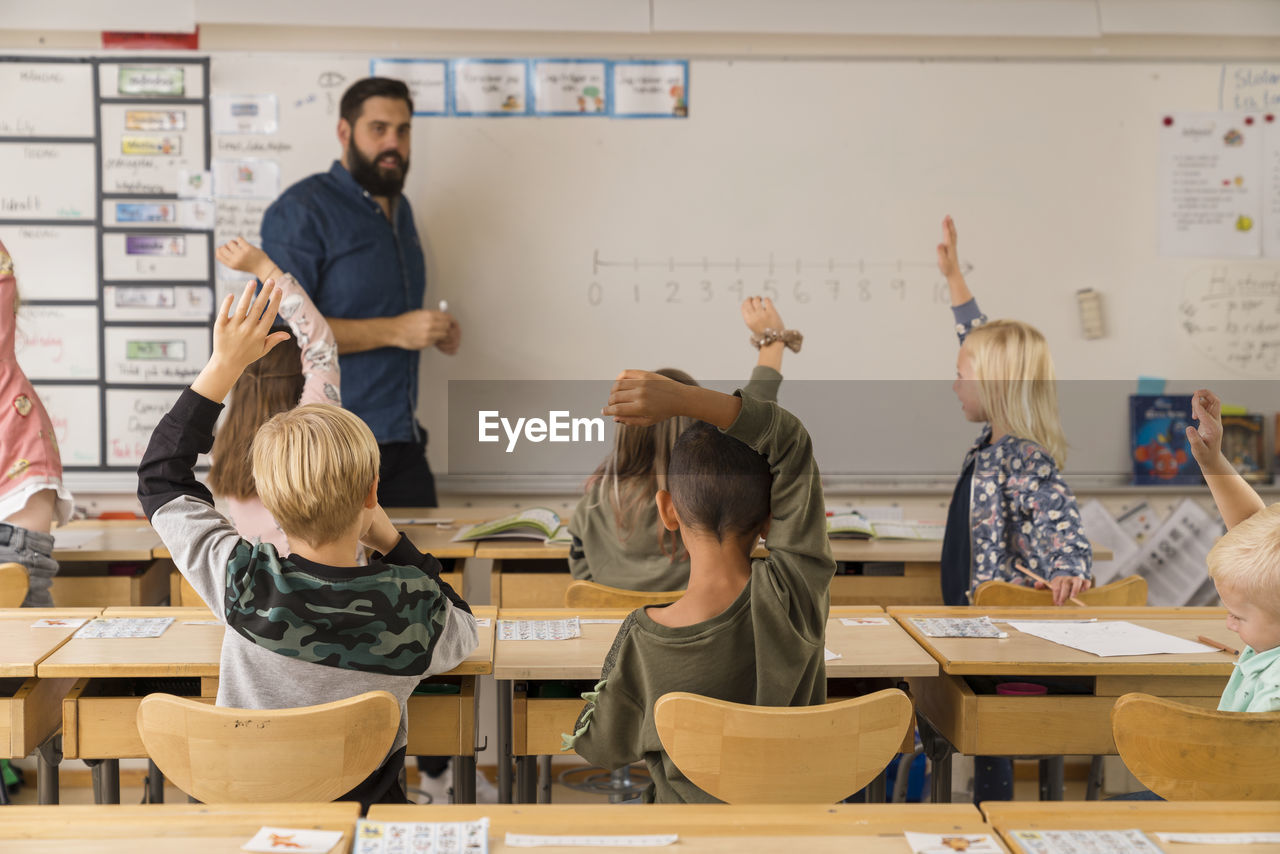 Children raising hands classroom