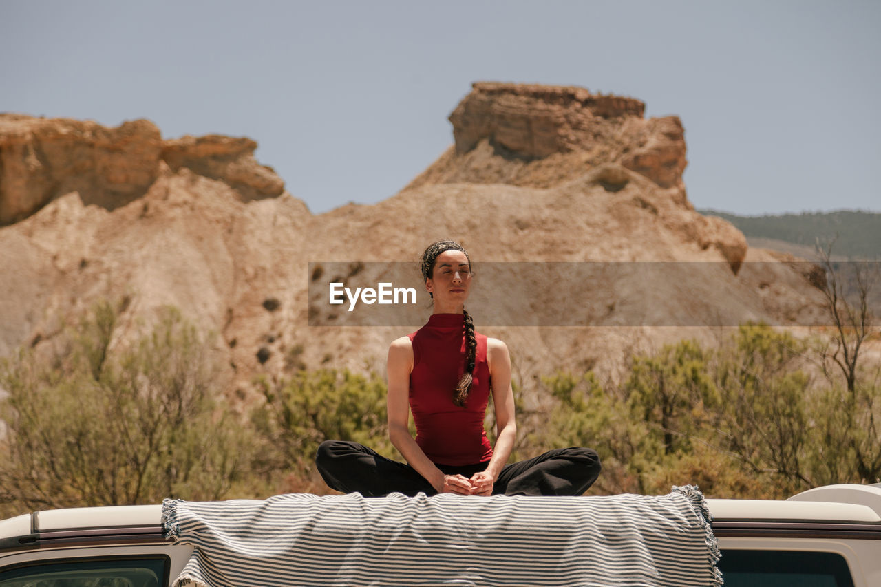 Low angle view of woman meditating while sitting on car roof