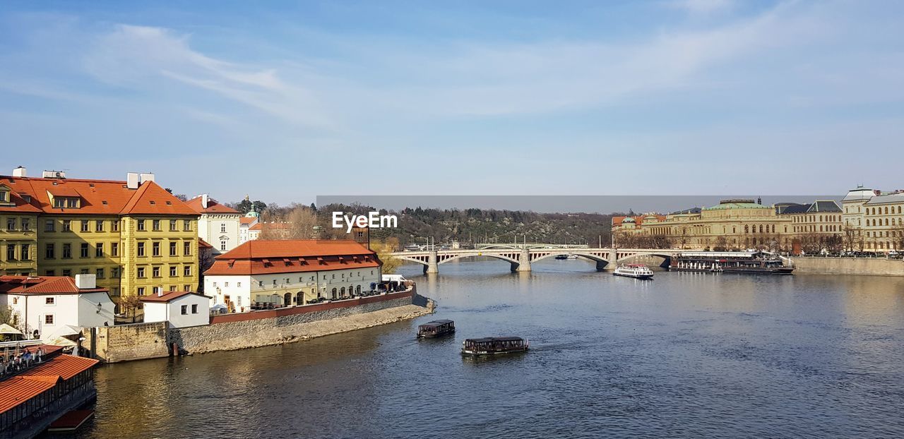 Bridge over river by buildings in city against sky