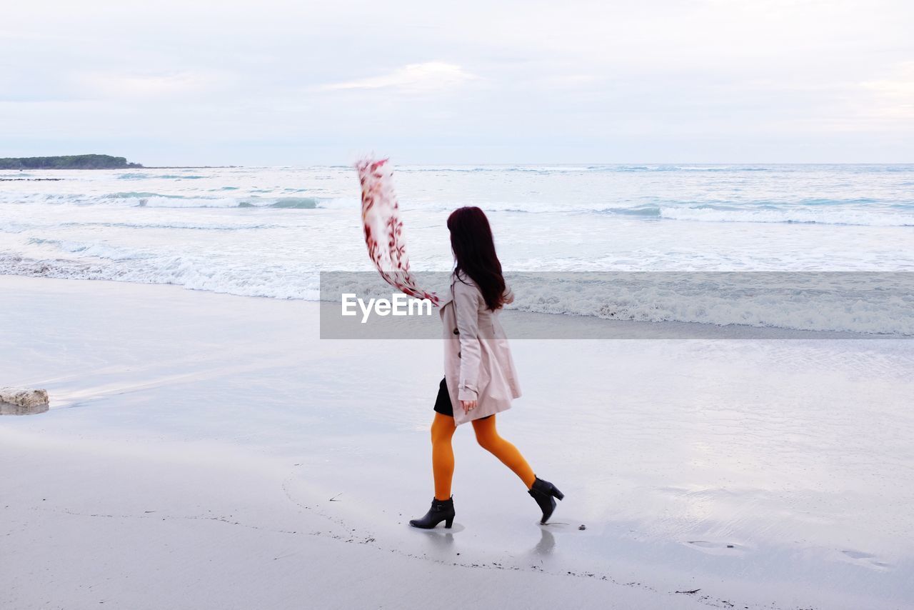 Woman walking on beach against sky
