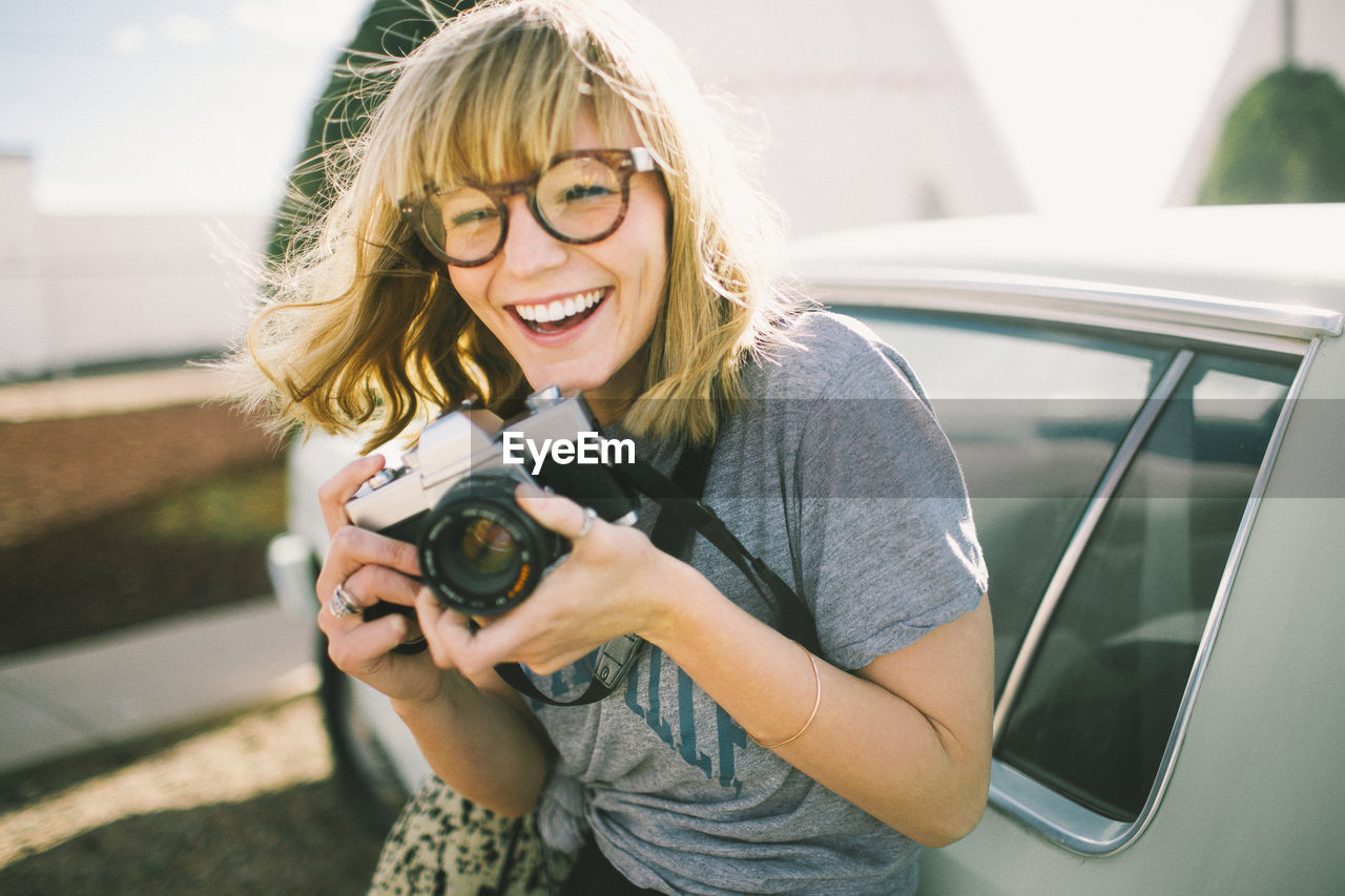 Happy teenager holding camera while standing by car