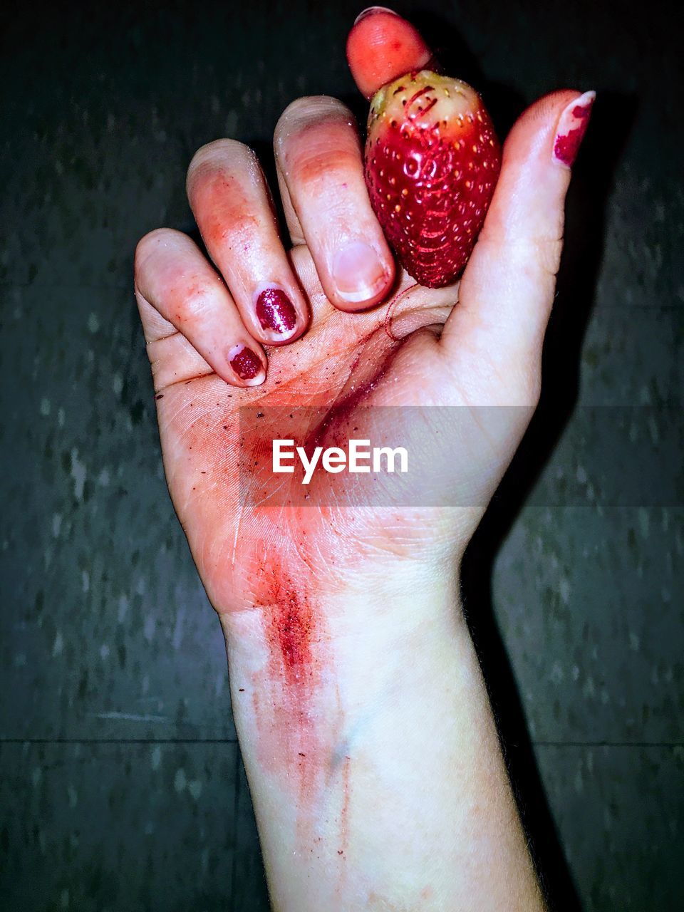 Close-up of bloody hand holding strawberry against wall