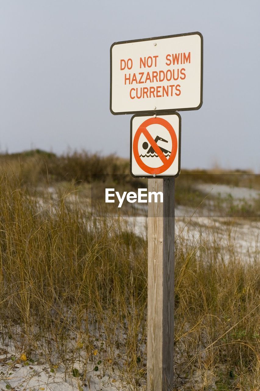 CLOSE-UP OF ROAD SIGN BY GRASS AGAINST SKY