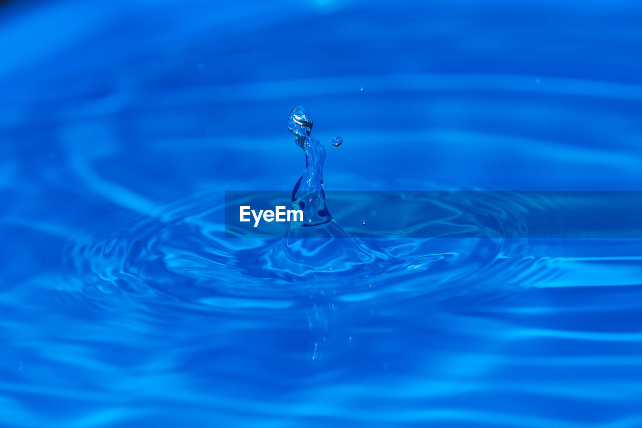 CLOSE-UP OF WATER DROP FALLING IN RIPPLED BLUE