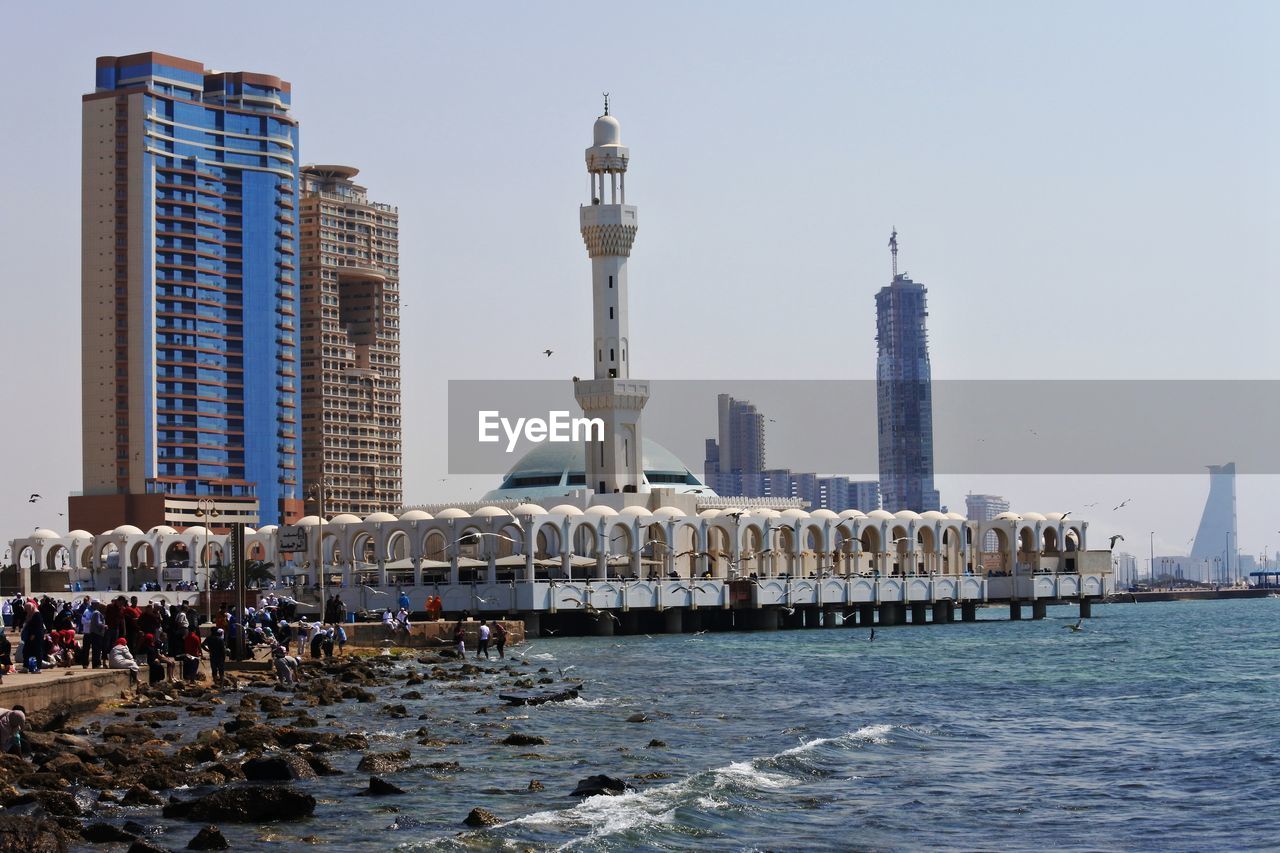 Mosque by sea against clear sky during sunny day