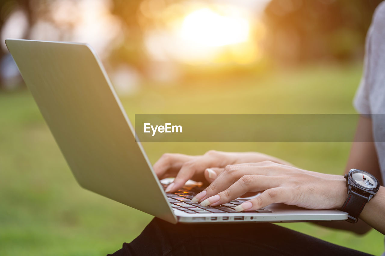 Midsection of woman using laptop at park