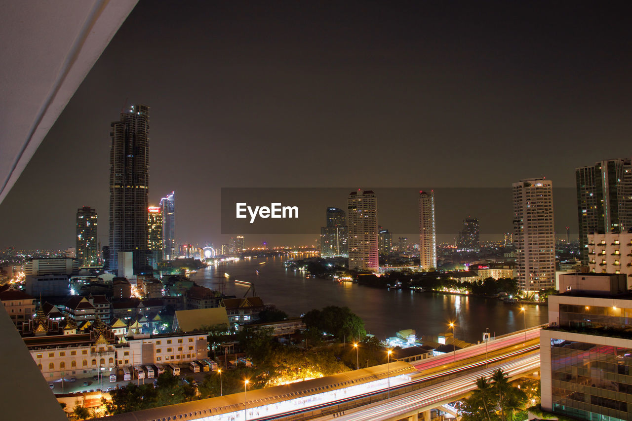 Illuminated modern buildings in city against sky at night