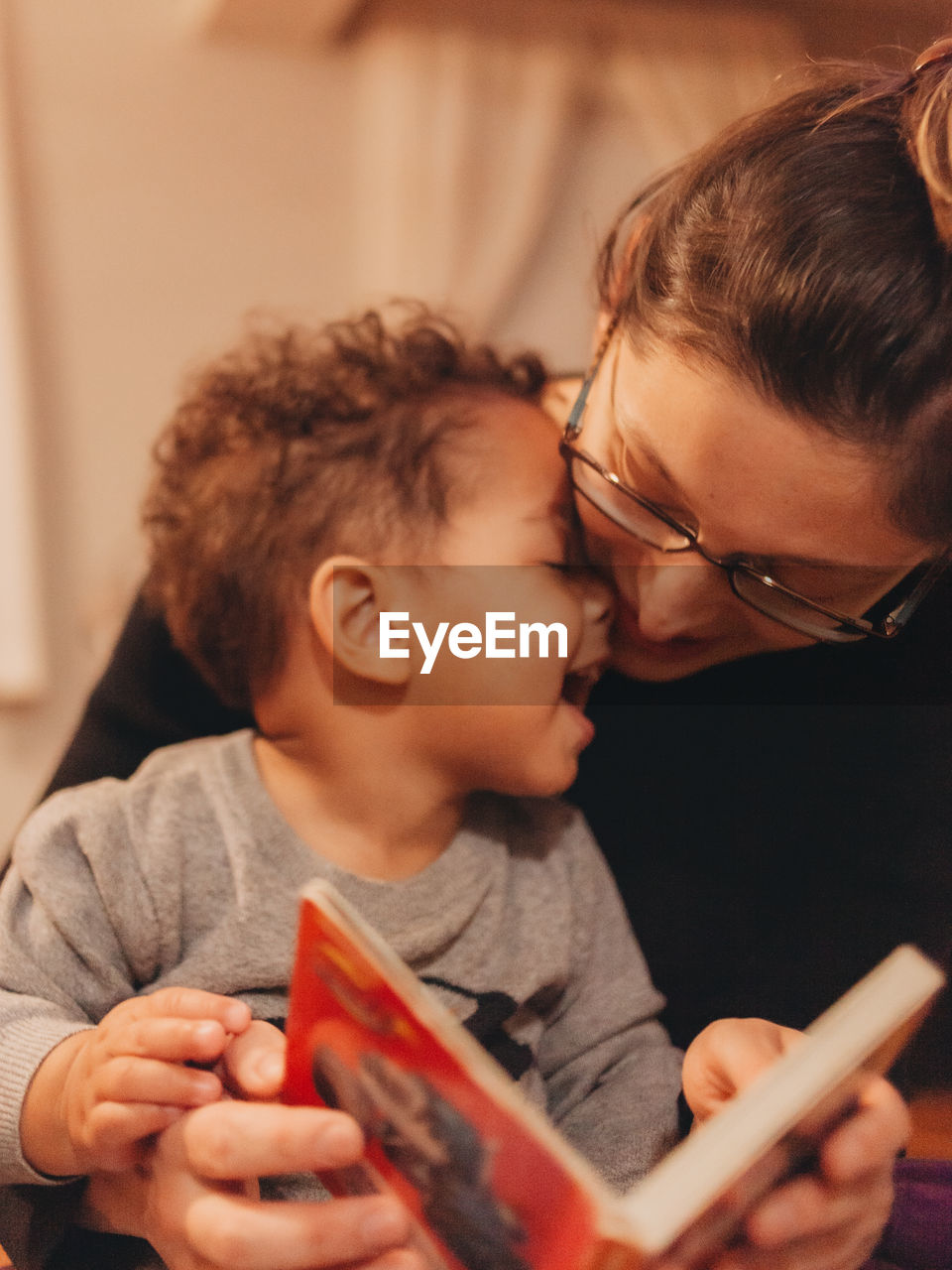 Close-up of mother reading book while sitting with playful boy at home