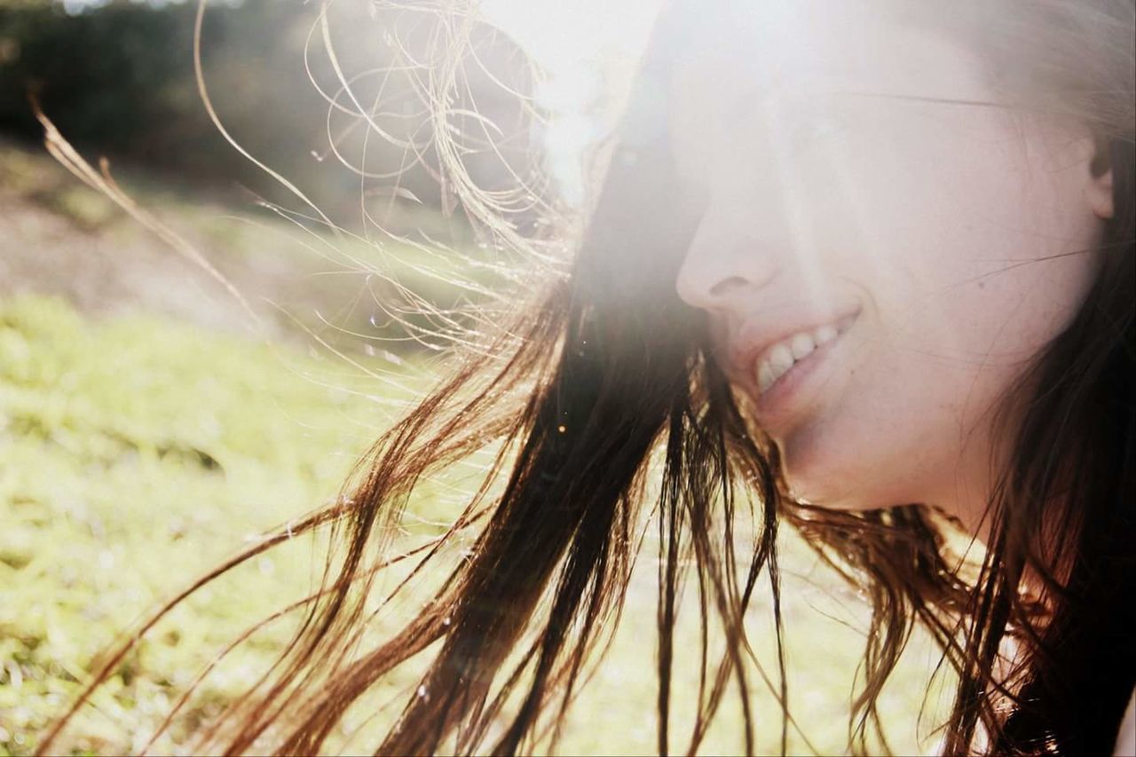 Close-up of smiling woman with tousled hair on sunny day