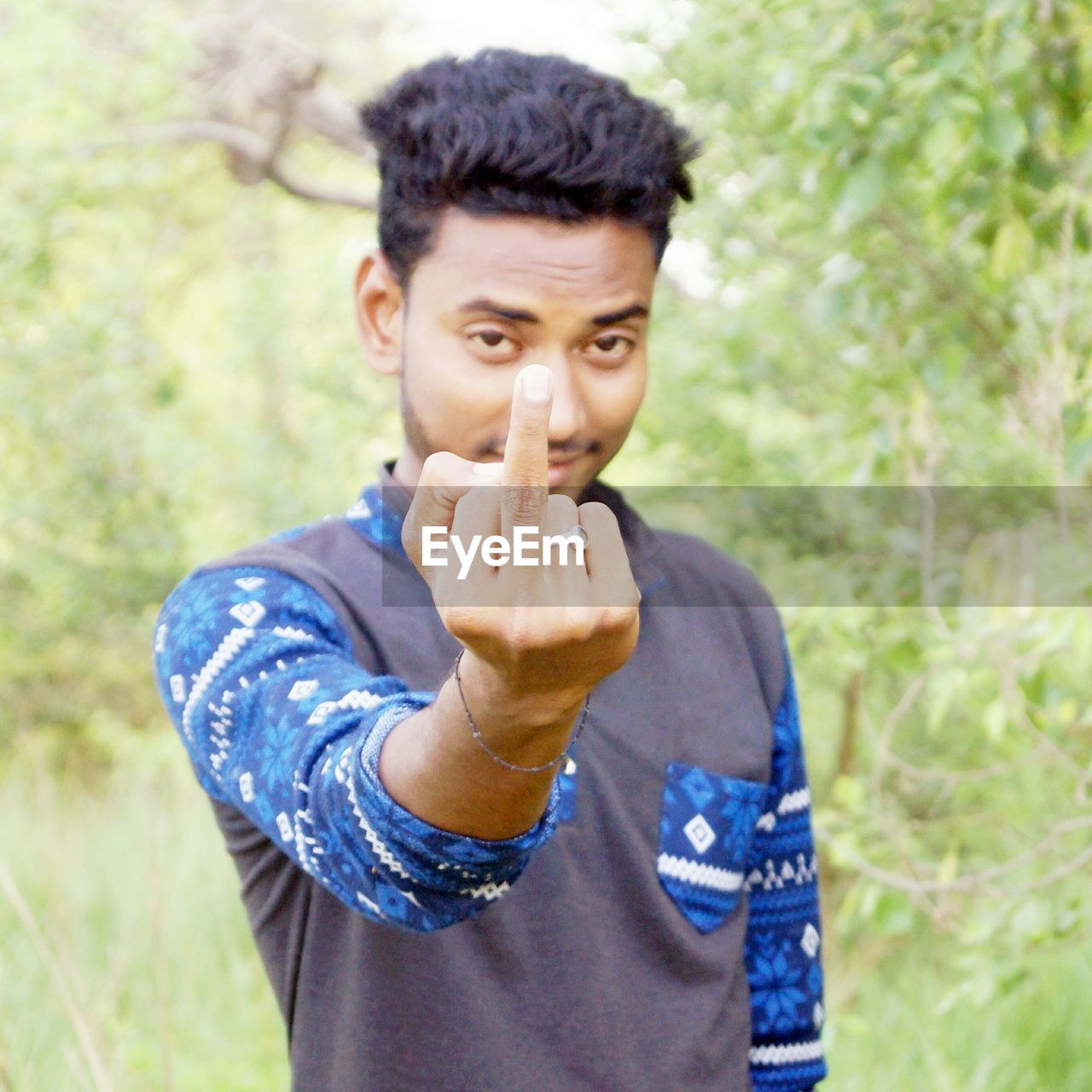 Portrait of young man showing middle finger while standing against plants