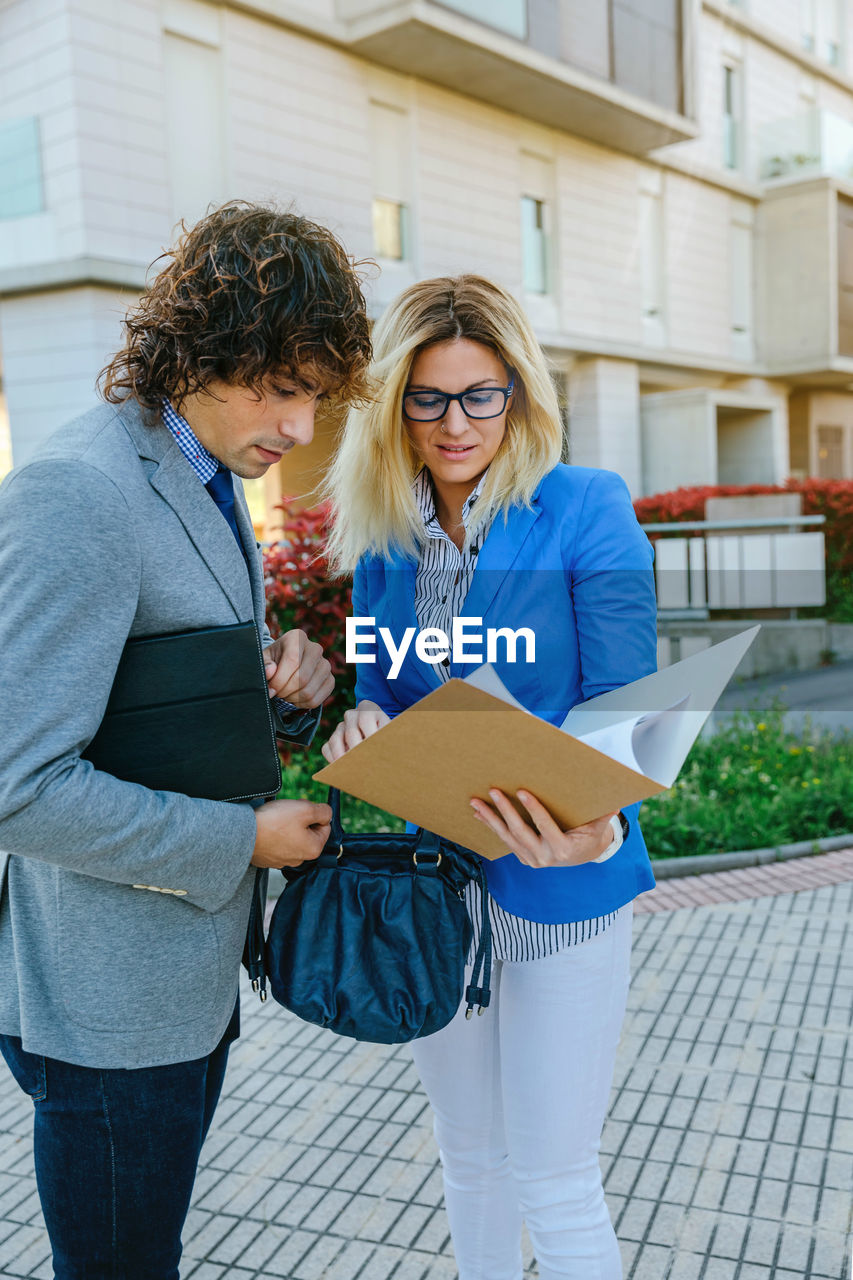 Business colleagues looking at file while standing against office building