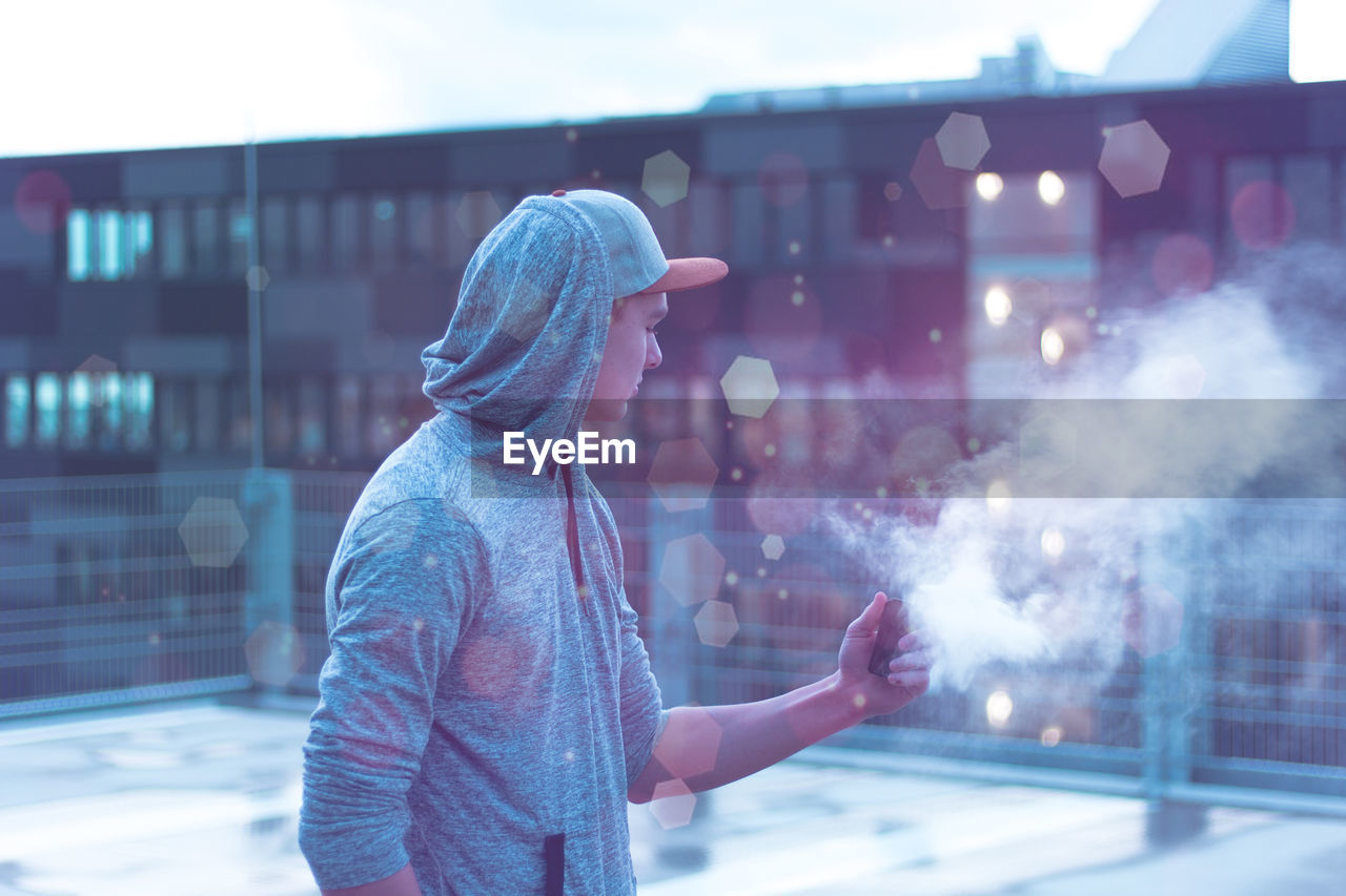 Side view of young man standing by smoke in city