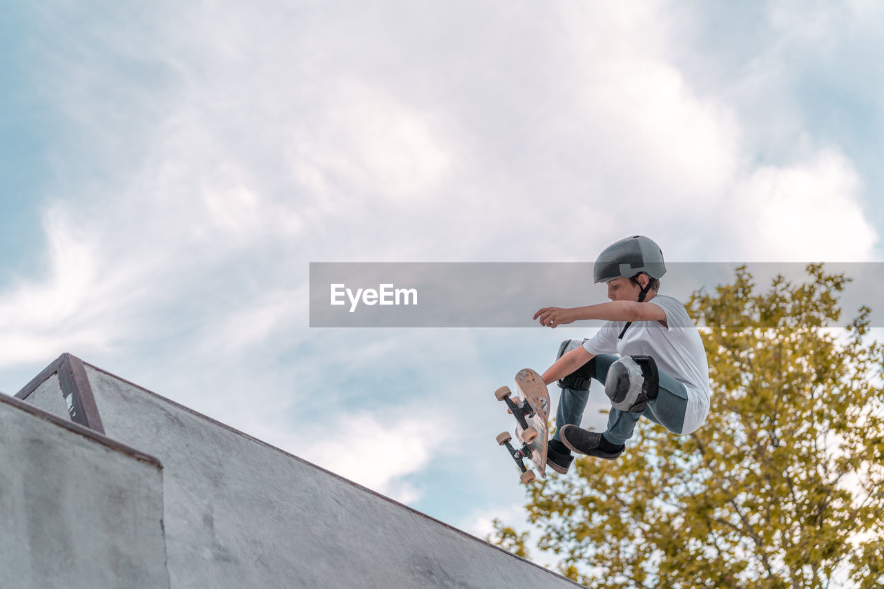 Teenage boy jumping with skateboard and showing stunt on ramp in skate park