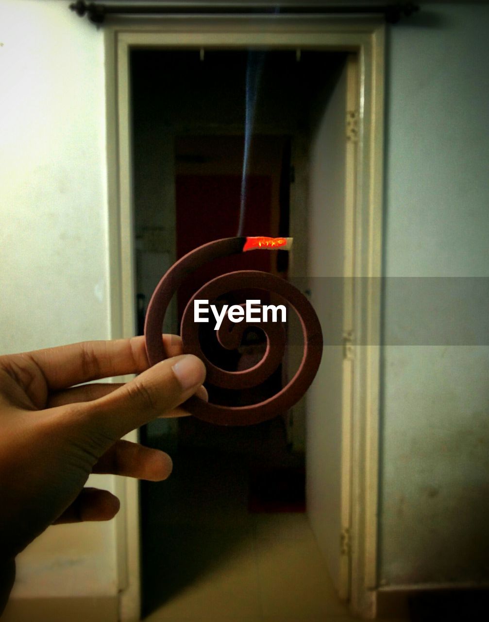 Cropped image of person holding mosquito coil at home