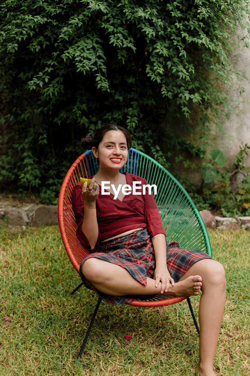 Portrait of smiling woman sitting against plants on field