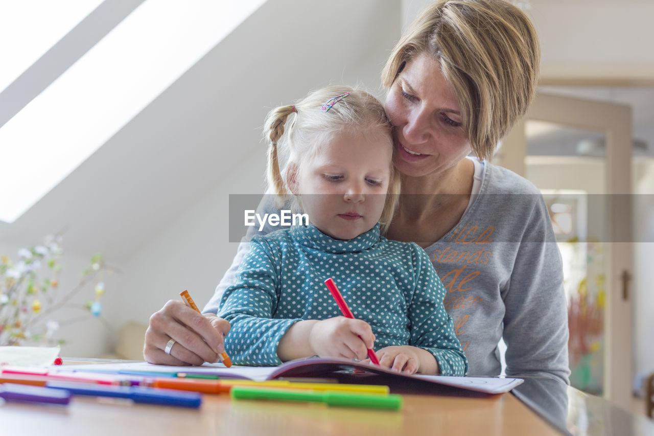 Mother and daughter coloring on book