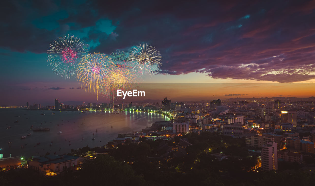 Firework display over illuminated city against sky at night