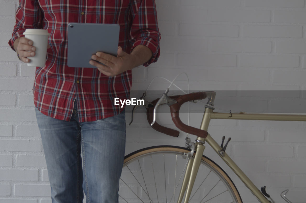 Hipster man with digital tablet and coffee next to bike