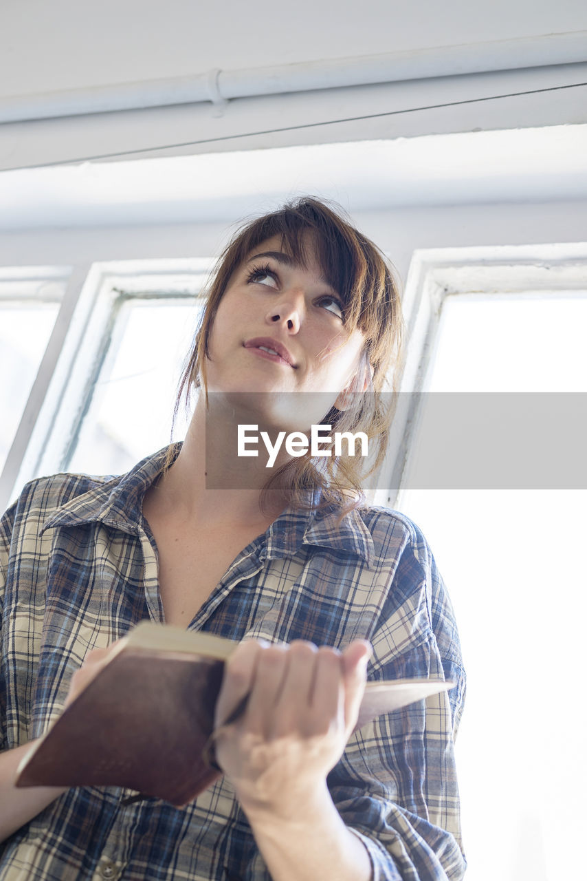 Young woman holding diary while looking up at home