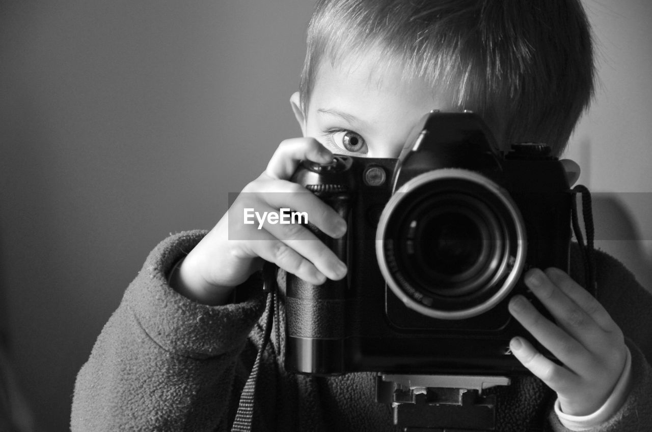 Close-up portrait of boy photographing with camera by wall