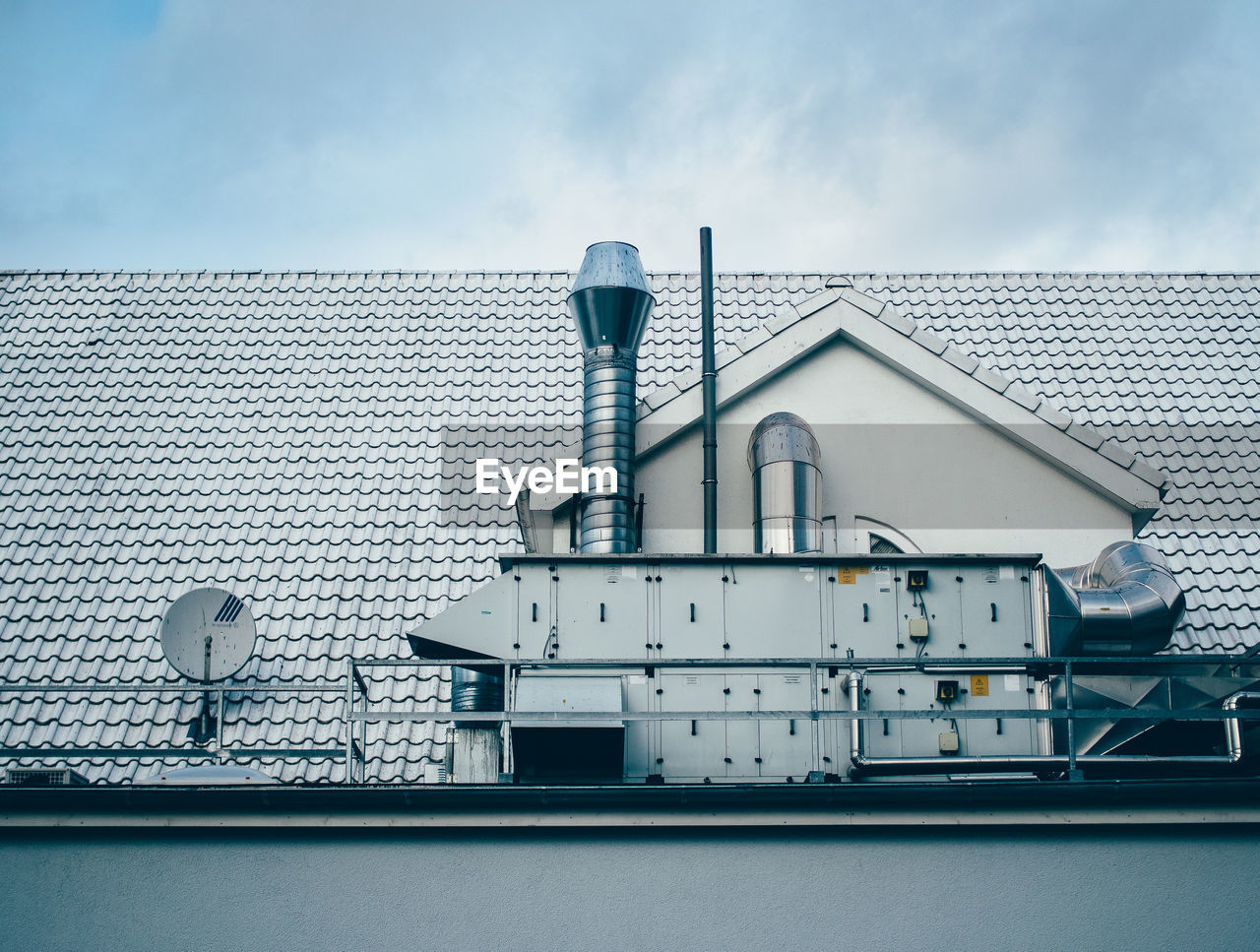 Low angel view of machinery on house rooftop against sky