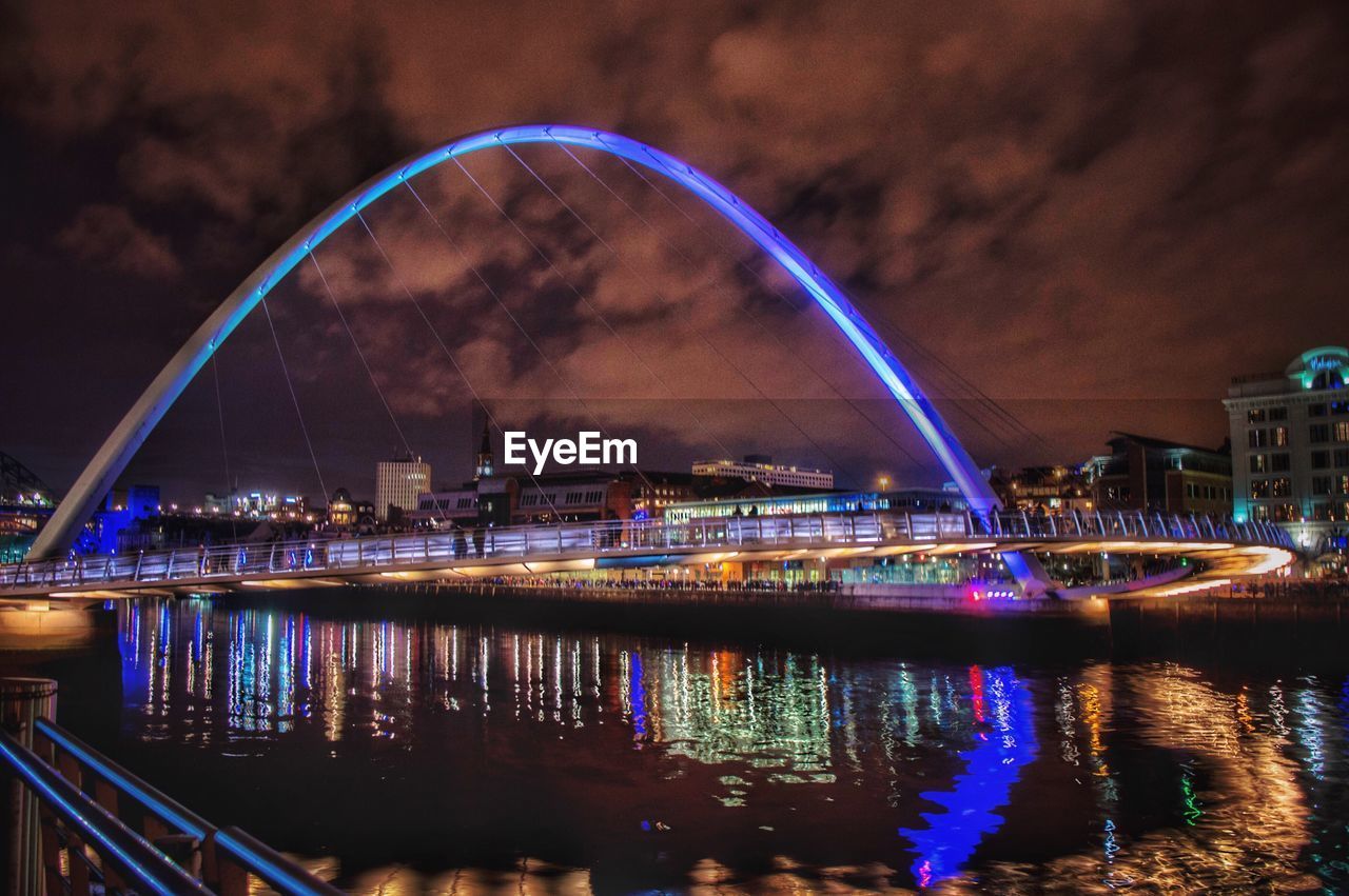 Illuminated bridge over river against sky at night