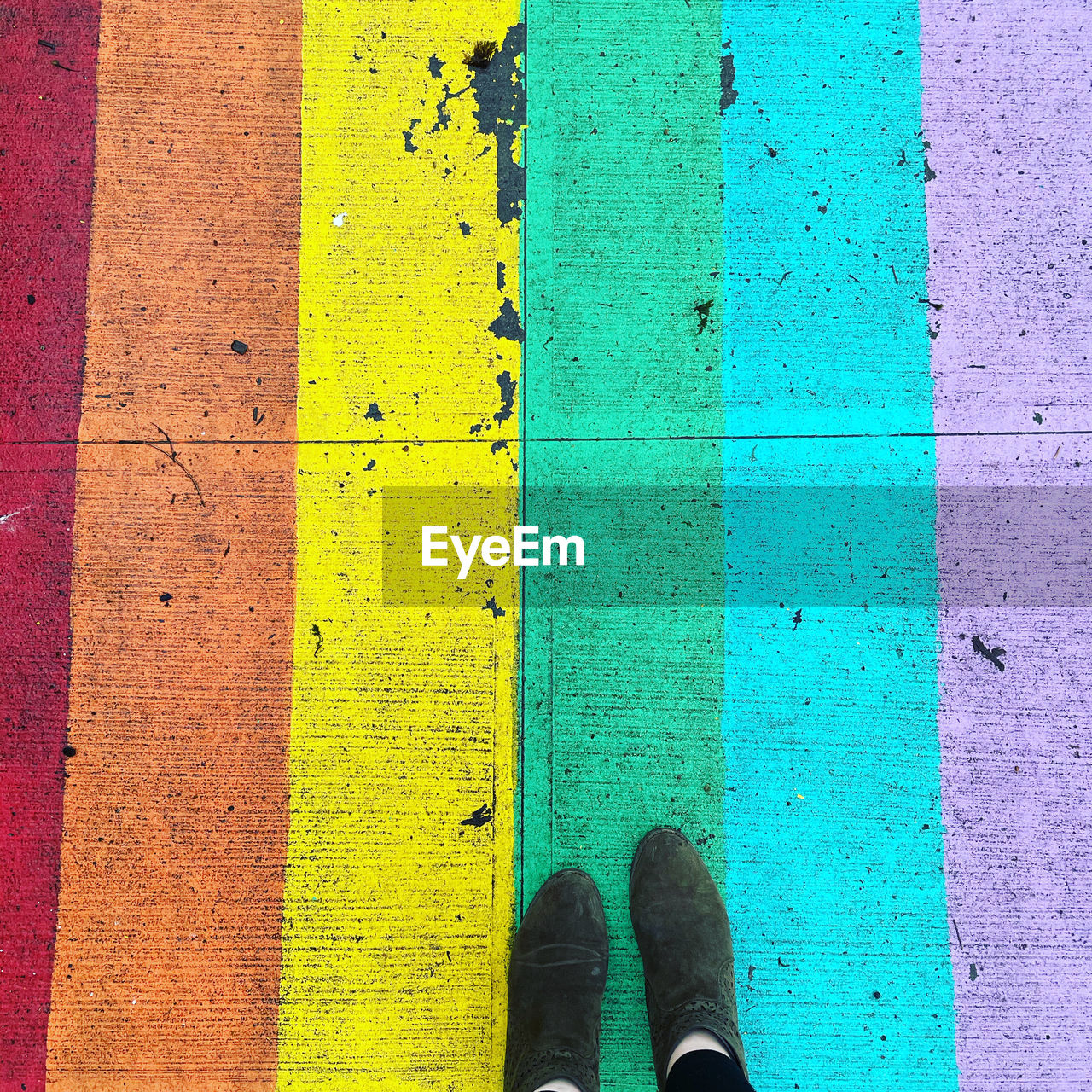 LOW SECTION OF PERSON STANDING BY MULTI COLORED SHOES ON WALL