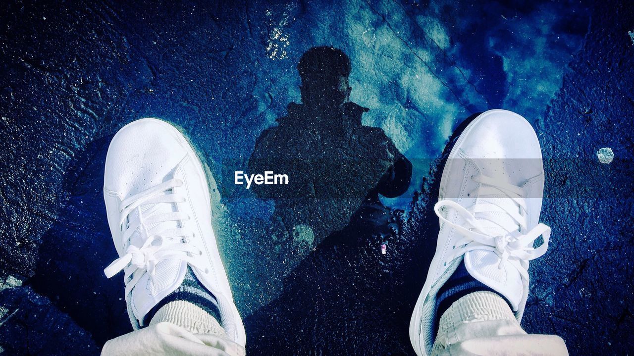 Low section of man standing on puddle with reflection