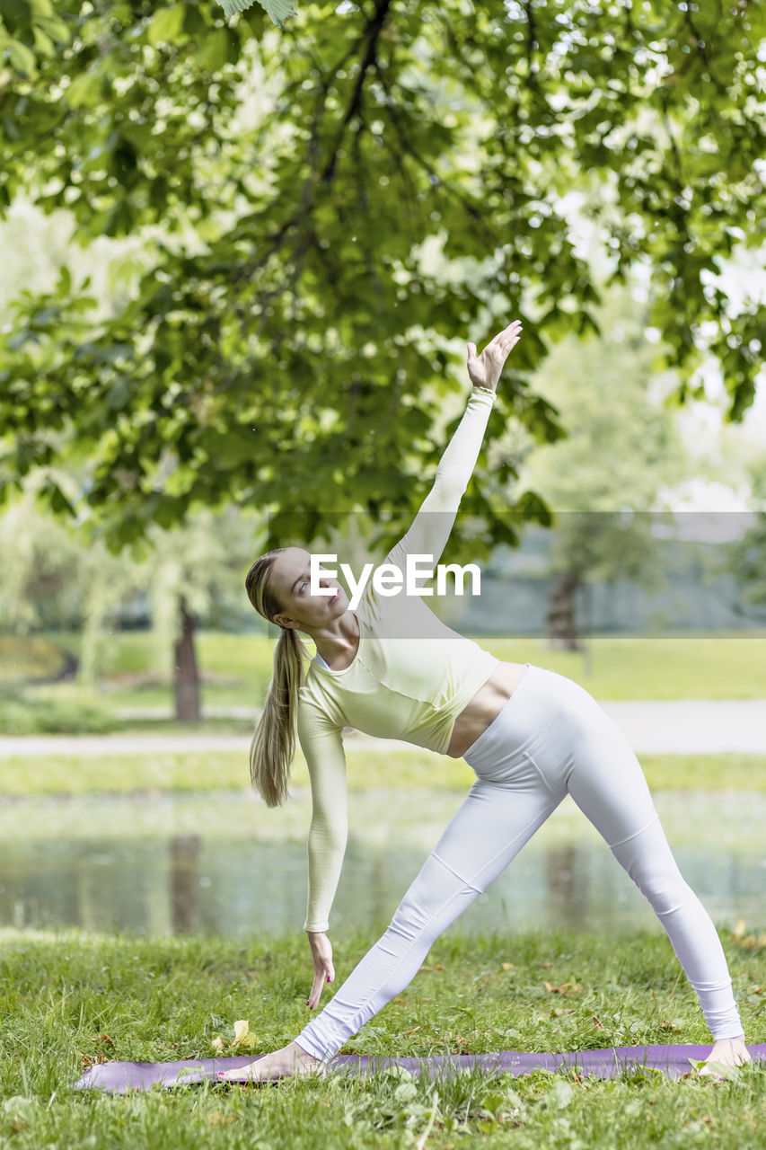 A young beautiful slender girl with long blonde hair does yoga in the summer in nature  in the park.