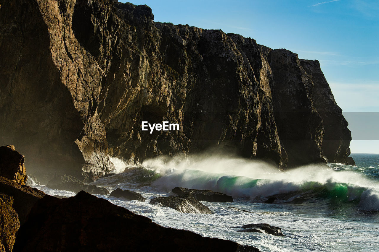 Sea waves splashing on rock against sky