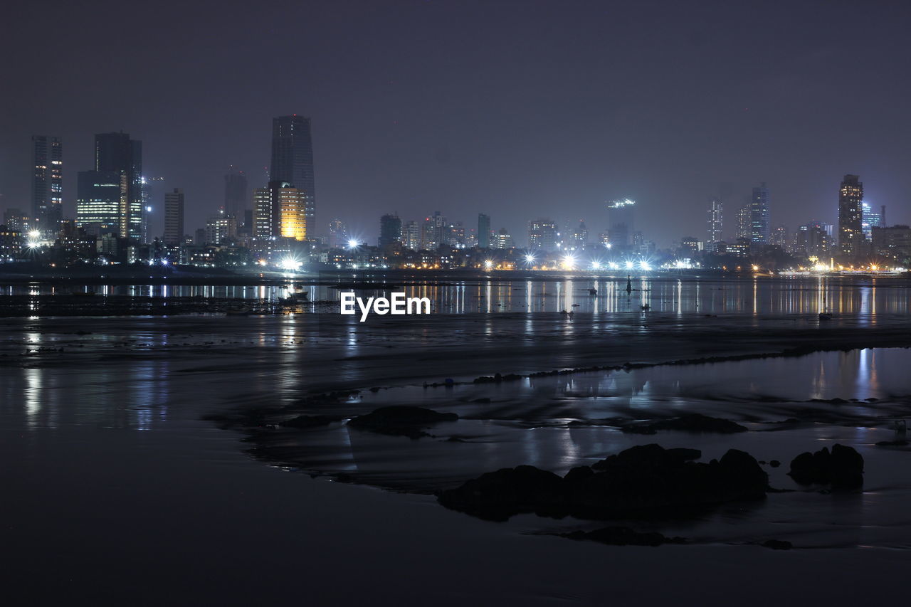 ILLUMINATED BUILDINGS BY RIVER AGAINST SKY