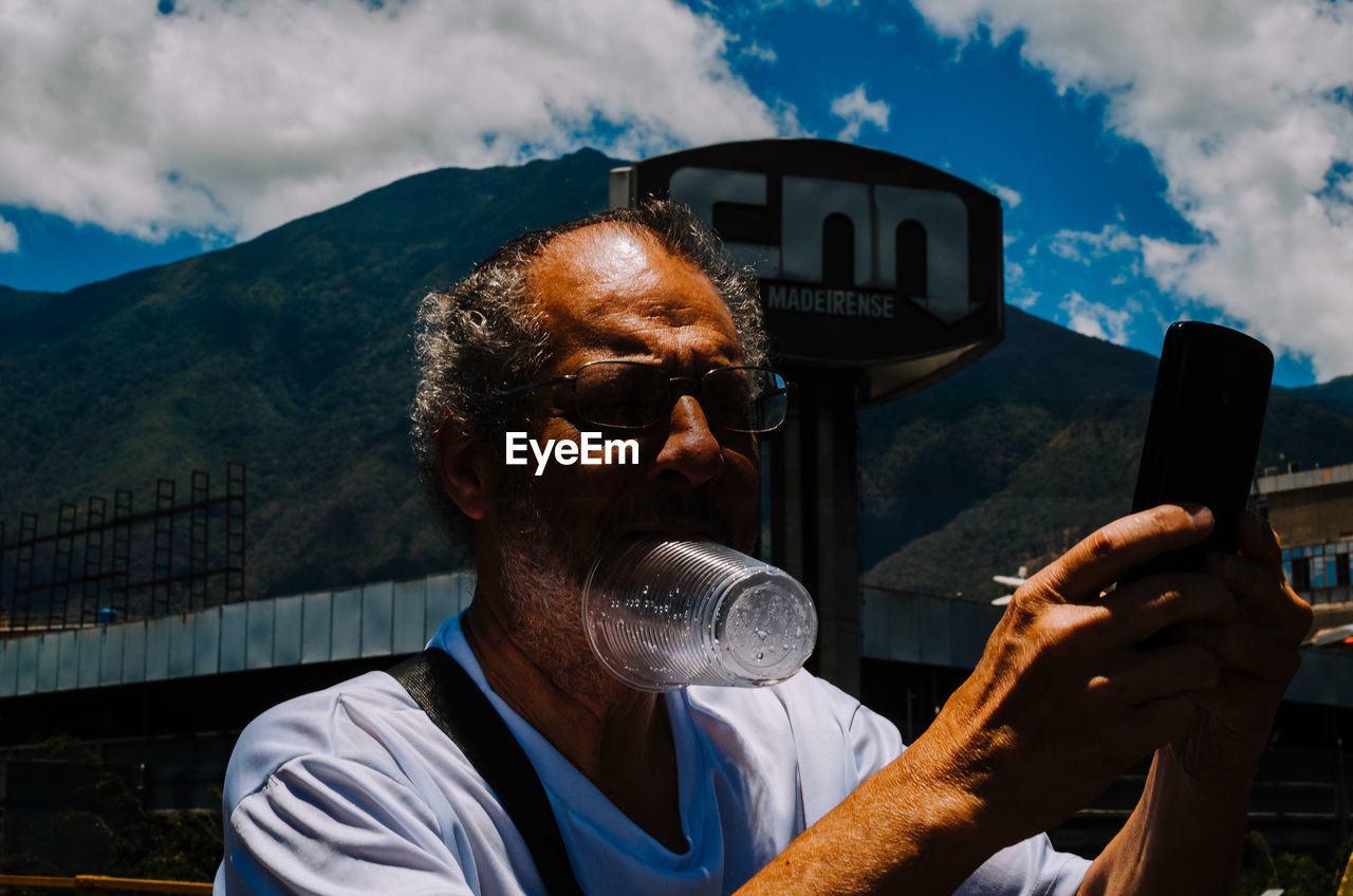 PORTRAIT OF MAN HOLDING CAMERA AGAINST SKY