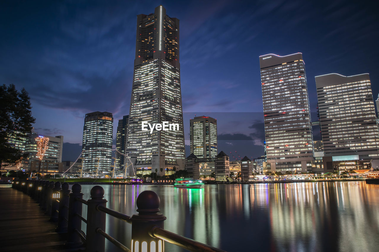 Illuminated buildings by river against sky in city of minato mirai, yokohama.