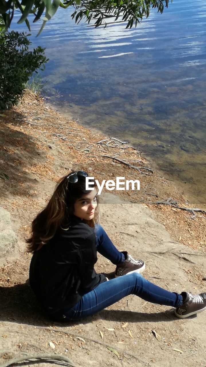 SIDE VIEW OF YOUNG WOMAN SITTING BY TREE