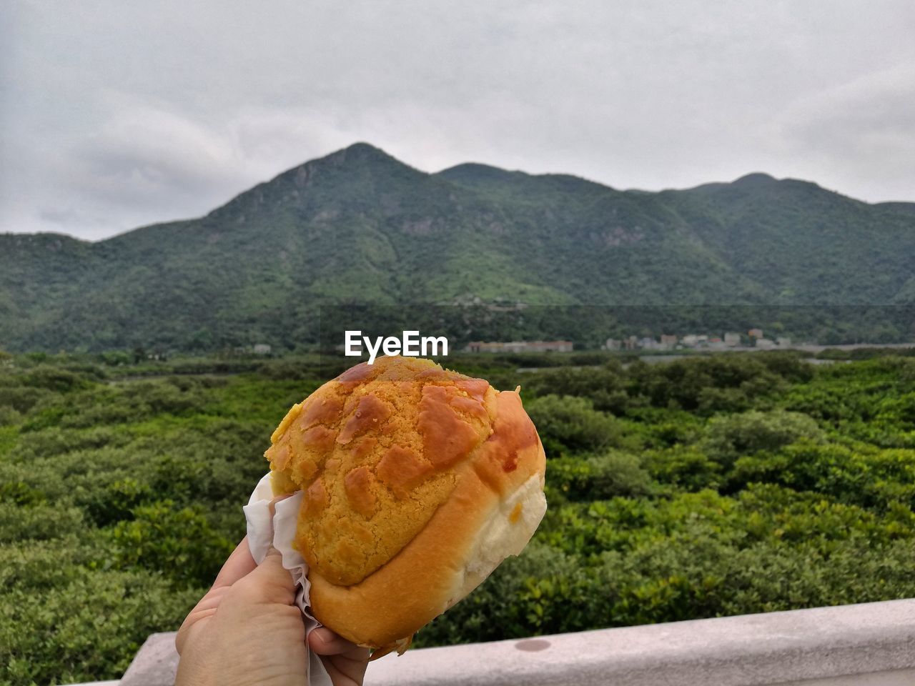 CLOSE-UP OF HAND HOLDING BREAD AGAINST MOUNTAINS