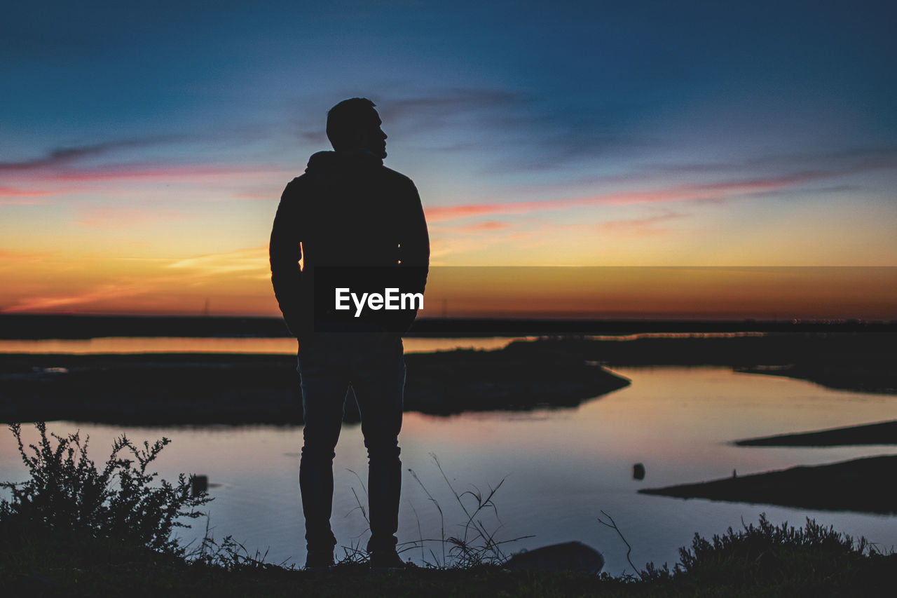 Rear view of man standing at beach during sunset