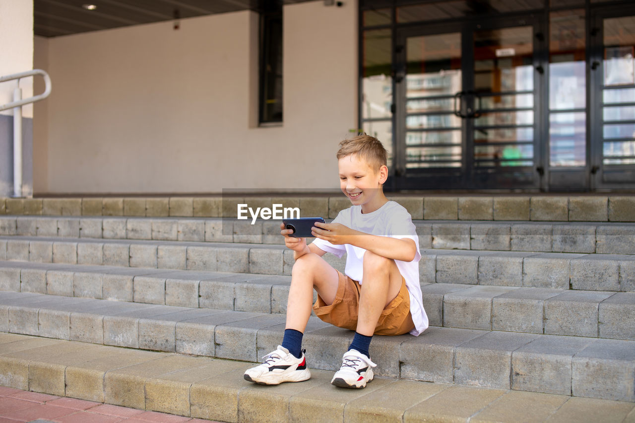 The boy sits on the steps and takes a selfie